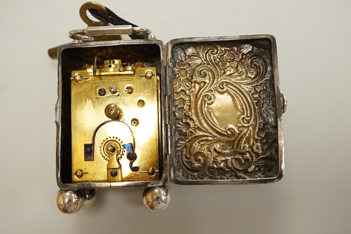 An early 20th century white metal (tests as silver) carriage timepiece, with white Roman dial (cracks) and case embossed with foliage, on four ball feet, 76mm excluding handle, with key.